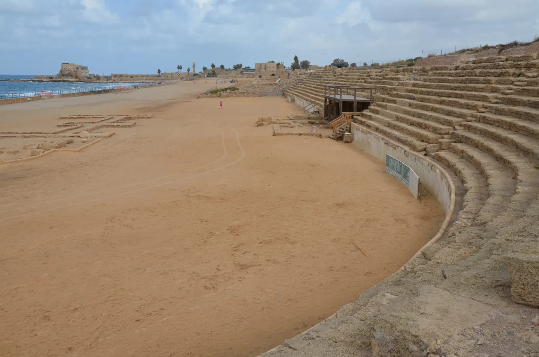 The sandy track of the hippodrome at Caesarea curving past its tiered stone seating, with the Mediterranean beyond