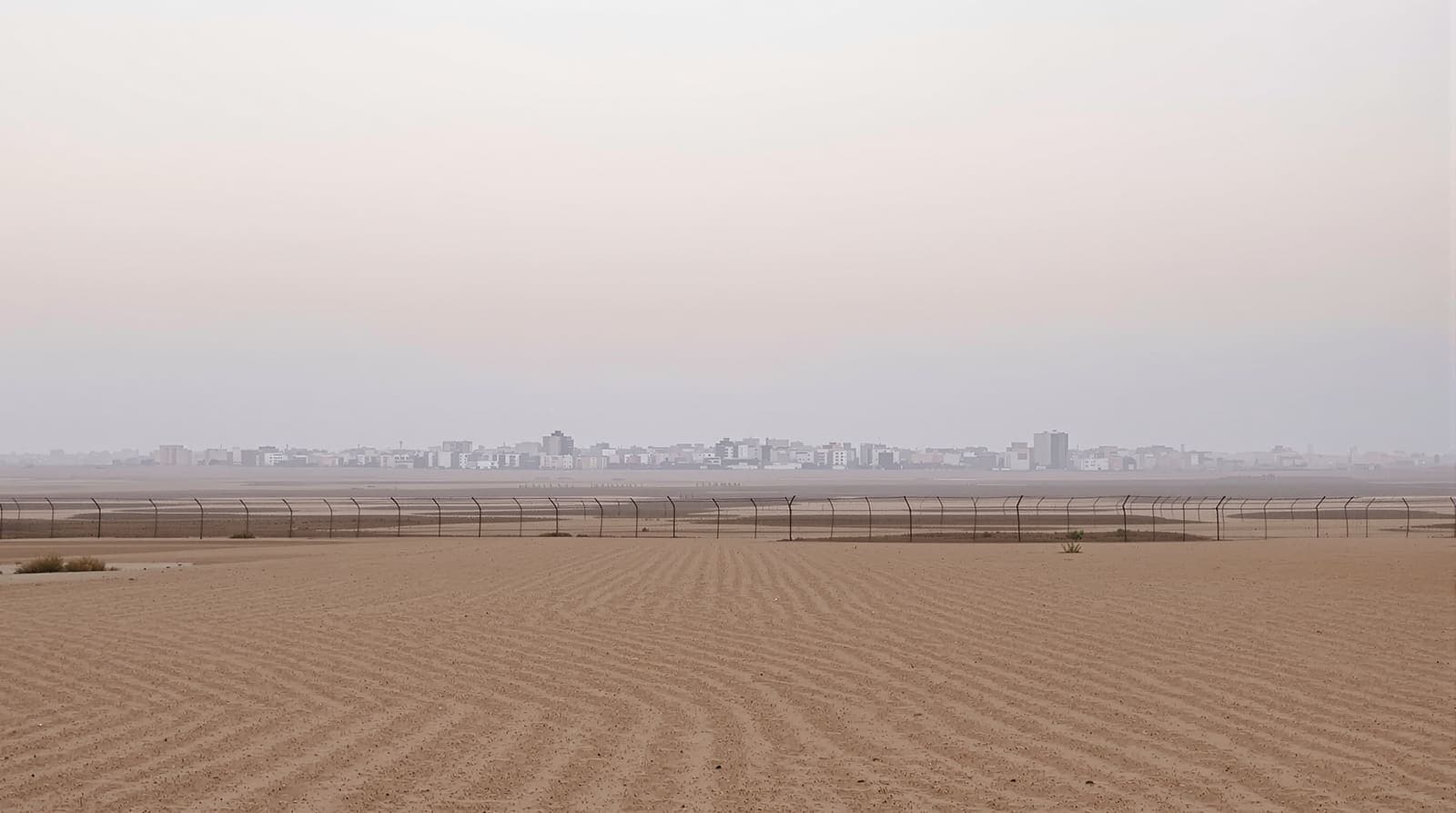 Illustration of the hazy southern Gaza skyline at dawn seen across sandy farmland beyond a long border fence