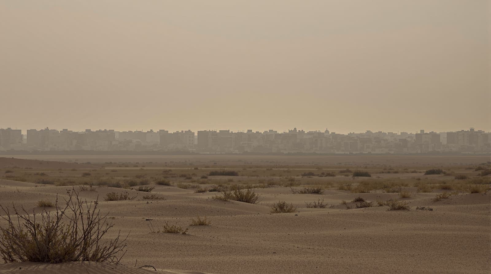 Illustration of a distant southern Gaza city skyline in dusty haze at dusk, seen across flat scrubland from far away.
