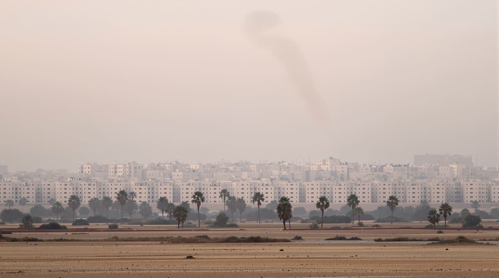 Illustration of the hazy low skyline of Khan Younis seen across flat sandy farmland at dawn