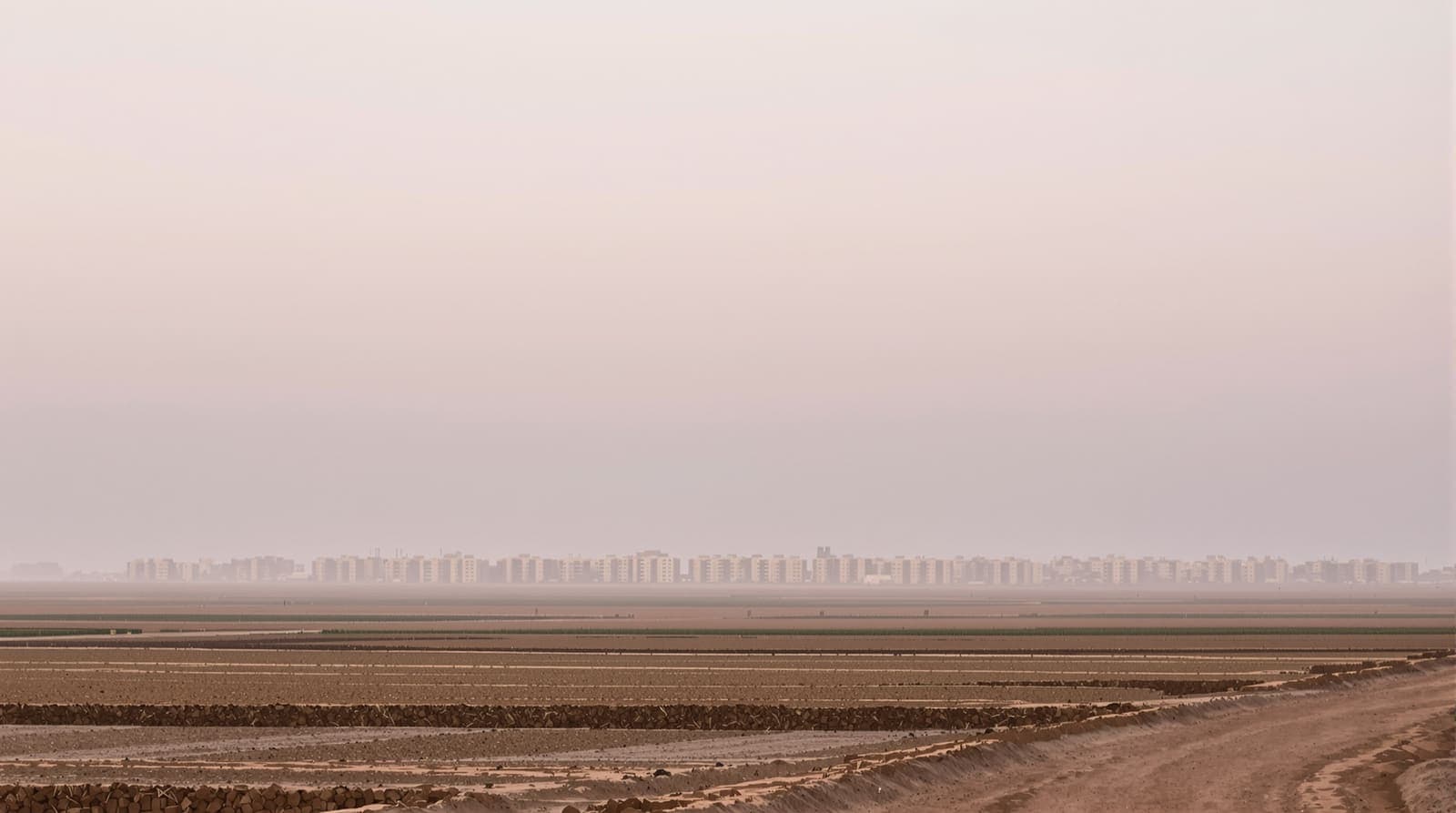 Illustration of the hazy Khan Yunis skyline at dawn seen across flat farmland in southern Gaza