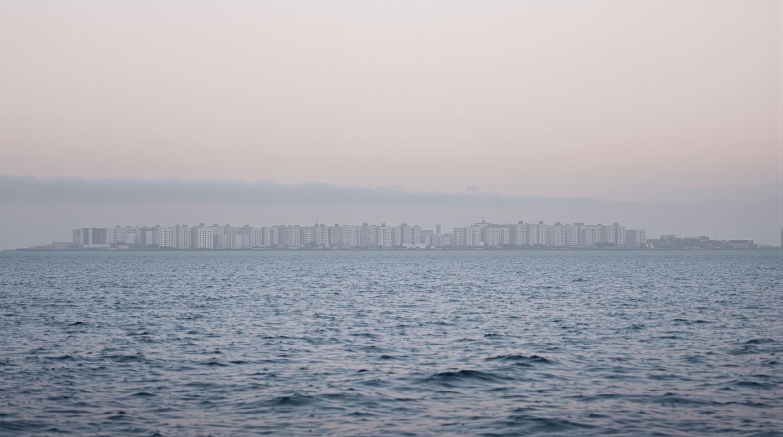 Illustration of the distant Gaza coastline seen across calm Mediterranean water at dawn, hazy and still.