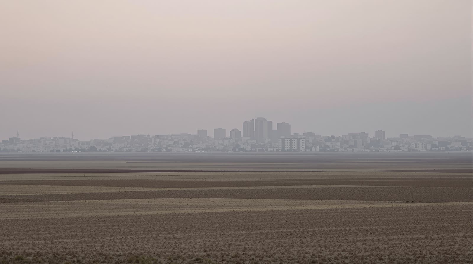 Illustration of the hazy skyline of northern Gaza City seen from distant farmland under an overcast dawn sky.