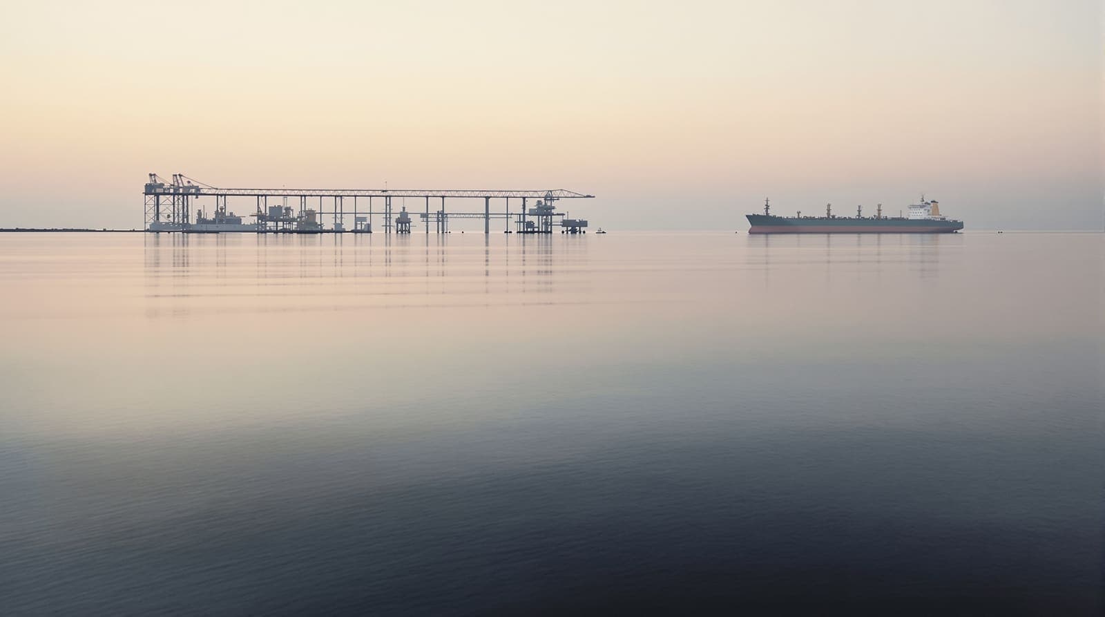Illustration of a distant offshore oil loading terminal and calm Gulf water under a hazy dawn sky.