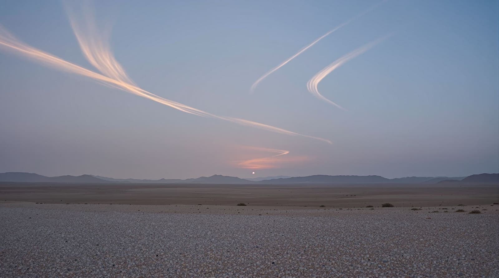 Illustration of a wide predawn desert horizon with faint high vapour trails catching first light above distant ridges.