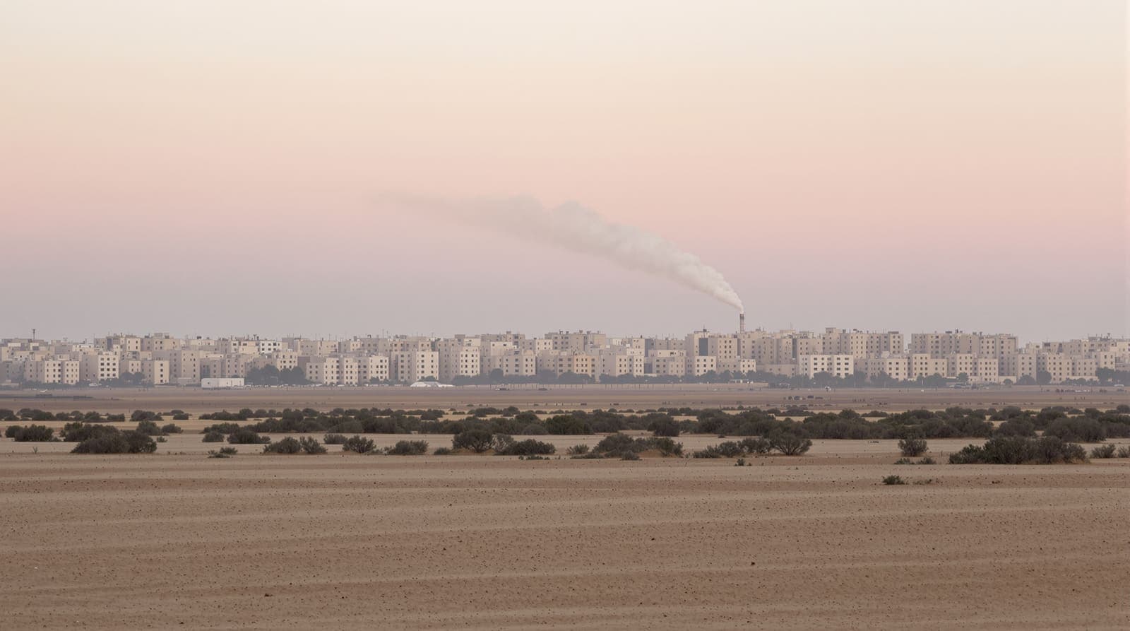 Illustration of the hazy low skyline of Khan Yunis seen across sandy farmland under an overcast dawn sky