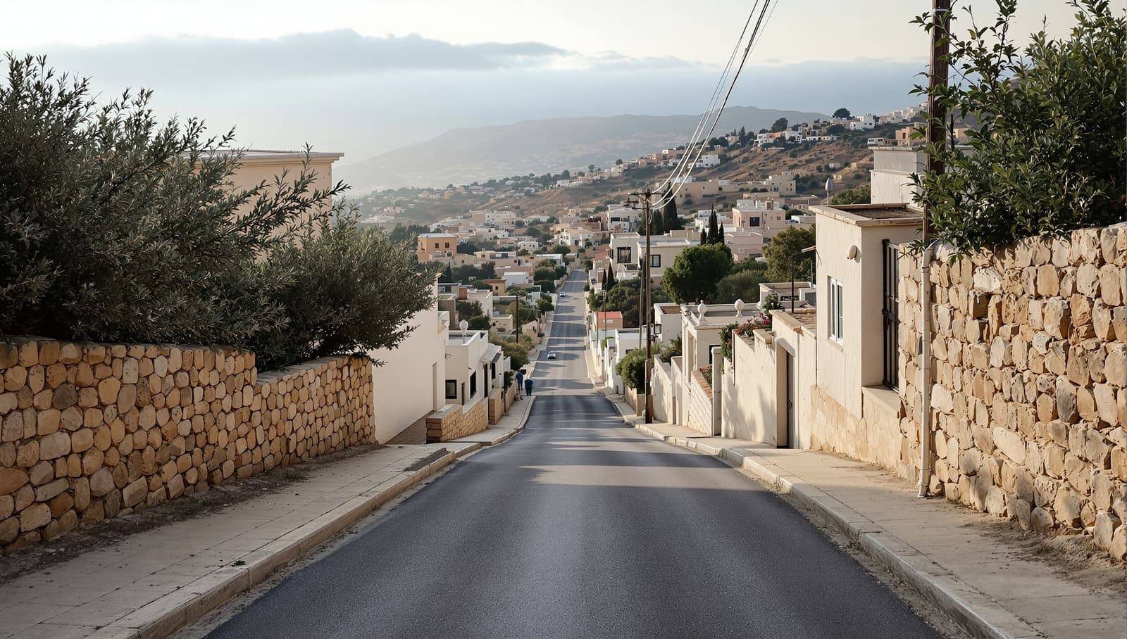Illustration of an empty stone-built hillside village lane at dawn, with olive terraces and hazy ridges beyond.
