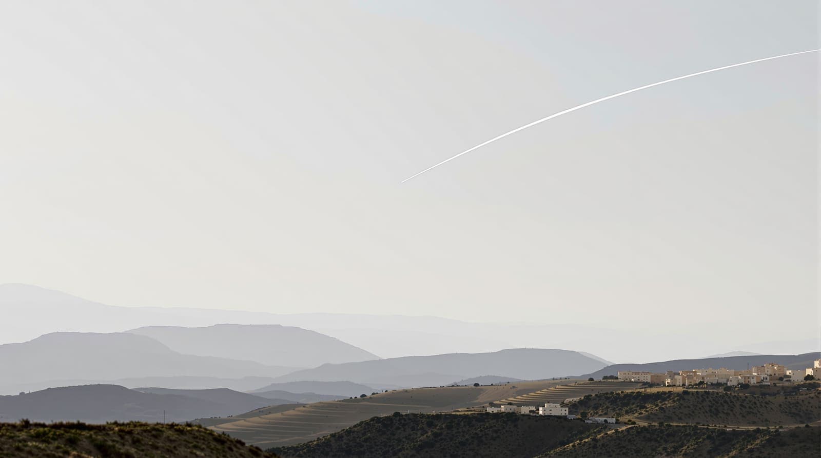 Illustration of a thin interceptor contrail curving into a pale dawn sky above the hazy terraced hills of southern Lebanon.