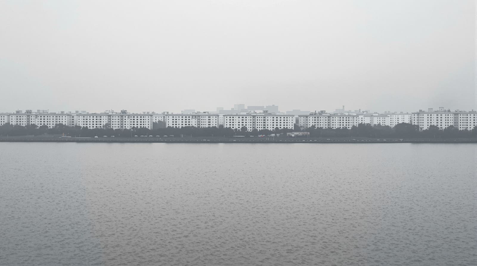 Illustration of the Zaporizhzhia skyline across the Dnipro river at an overcast dawn, with haze over the distant apartment blocks.
