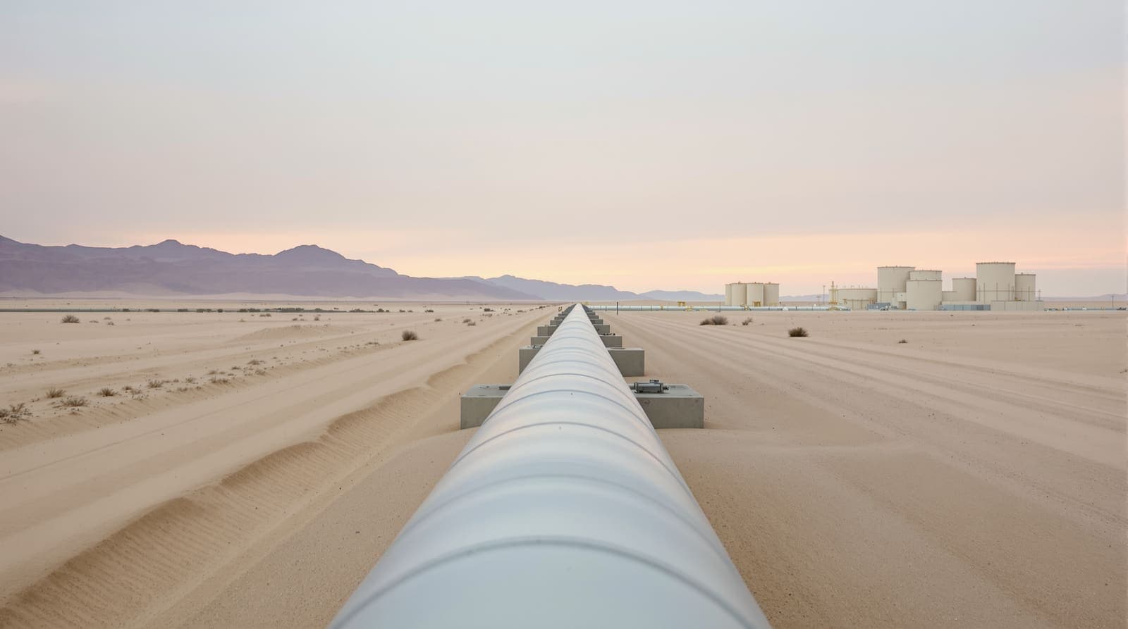 Illustration of a steel oil pipeline crossing open desert toward a distant pumping station under a pale dawn sky.