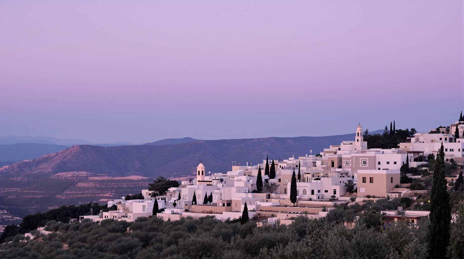 Illustration of a Galilee hillside town of terraced stone houses among olive groves at dusk.