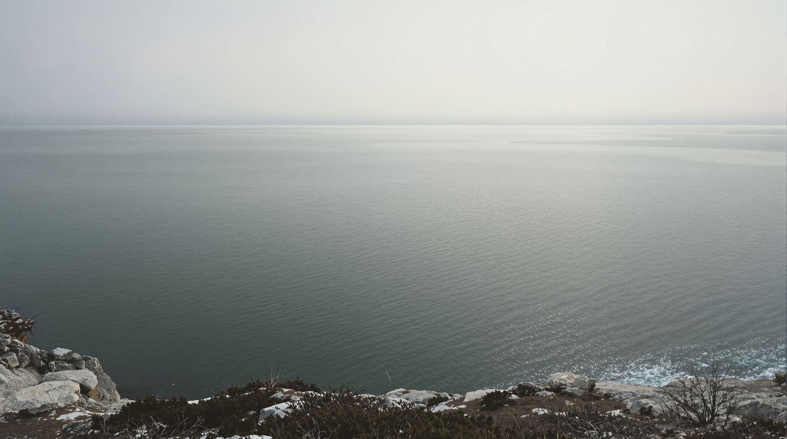 Illustration of calm grey Black Sea waters off Bulgaria's rocky coast at dawn, with a faint sheen on the surface under an overcast sky.
