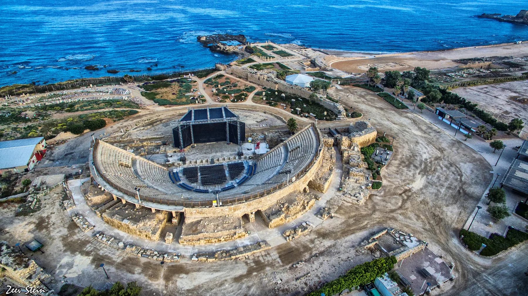The semicircular stone seating of the Roman theatre at Caesarea seen from above, with the Mediterranean beyond the stage