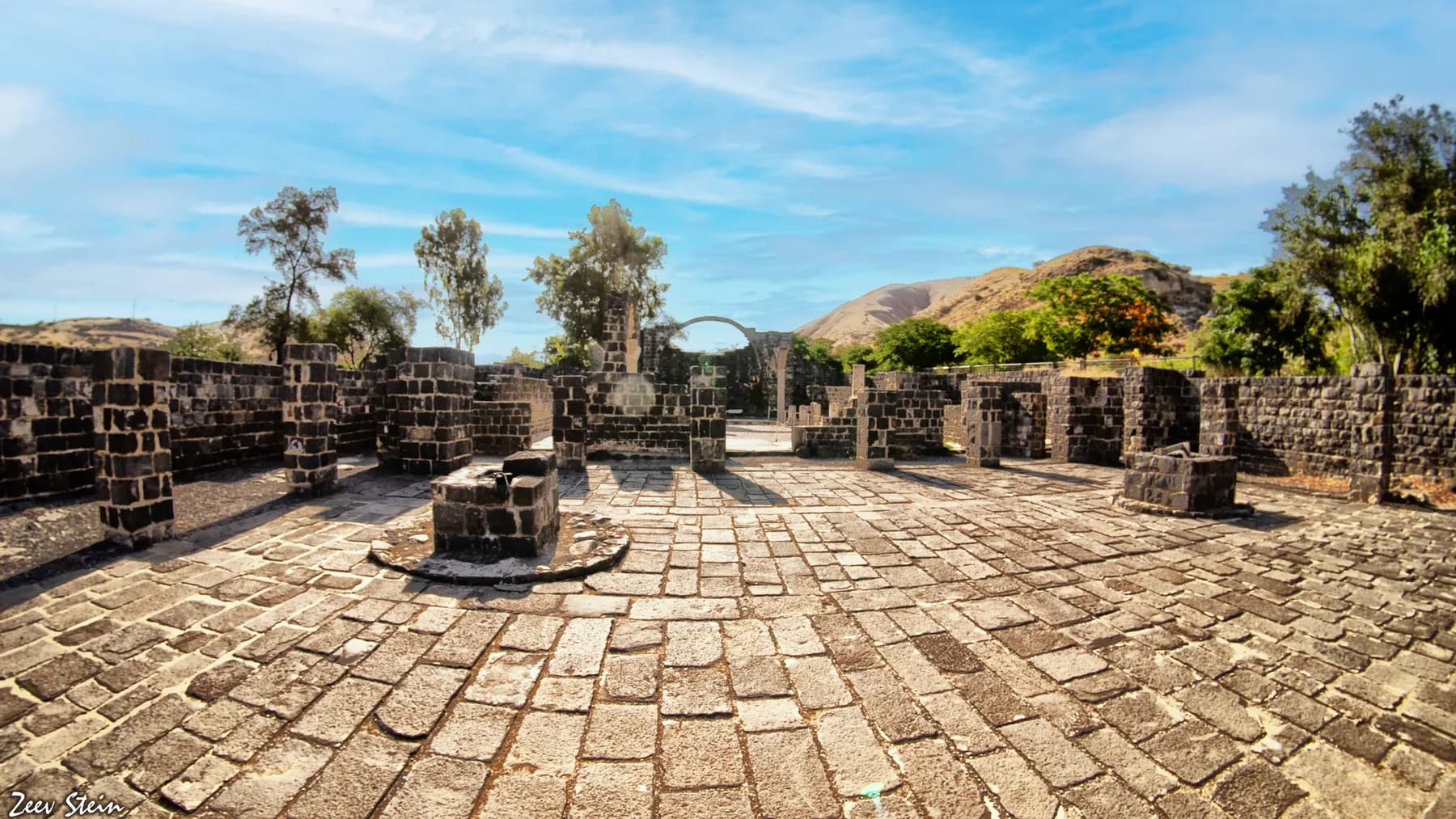The stone-paved floor and low basalt walls of the ruined Byzantine church at Kursi, with an arched doorway and dry hills beyond