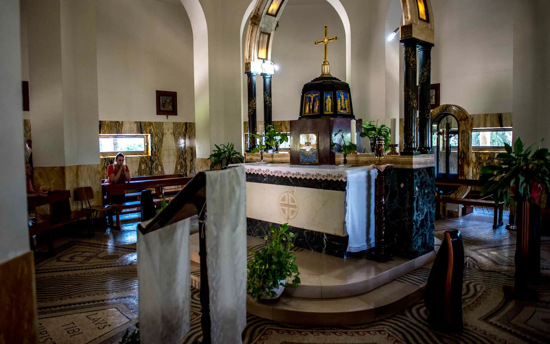 The white-draped altar of the Church of the Beatitudes beneath its dark painted canopy topped by a gilded dome and cross, with marble-clad piers and a mosaic floor around it