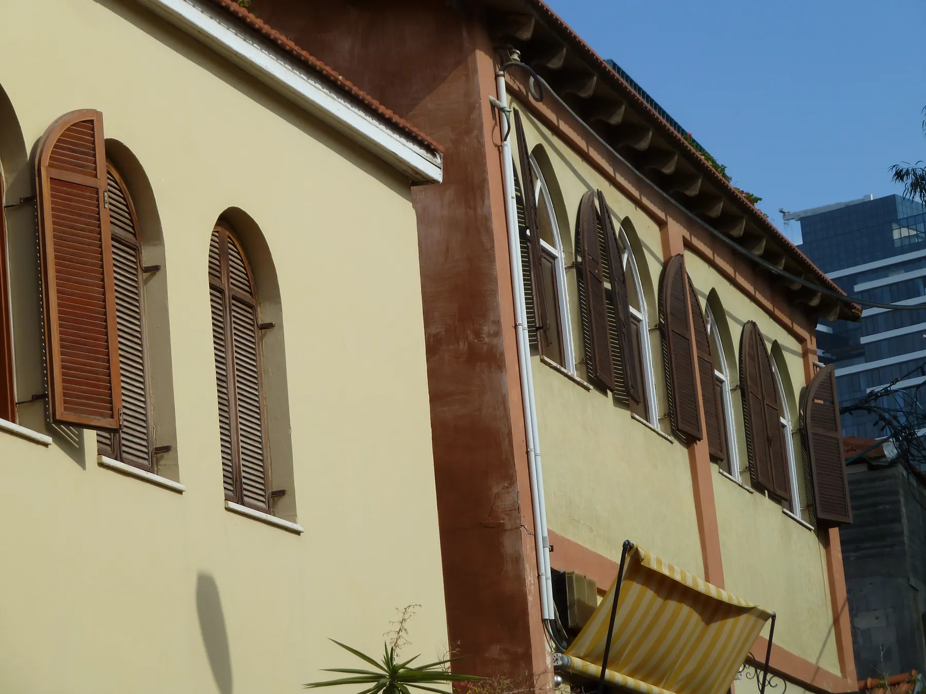 Two restored houses in Neve Tzedek seen from the street below, with tall arched wooden shutters, cream and terracotta render and tiled eaves