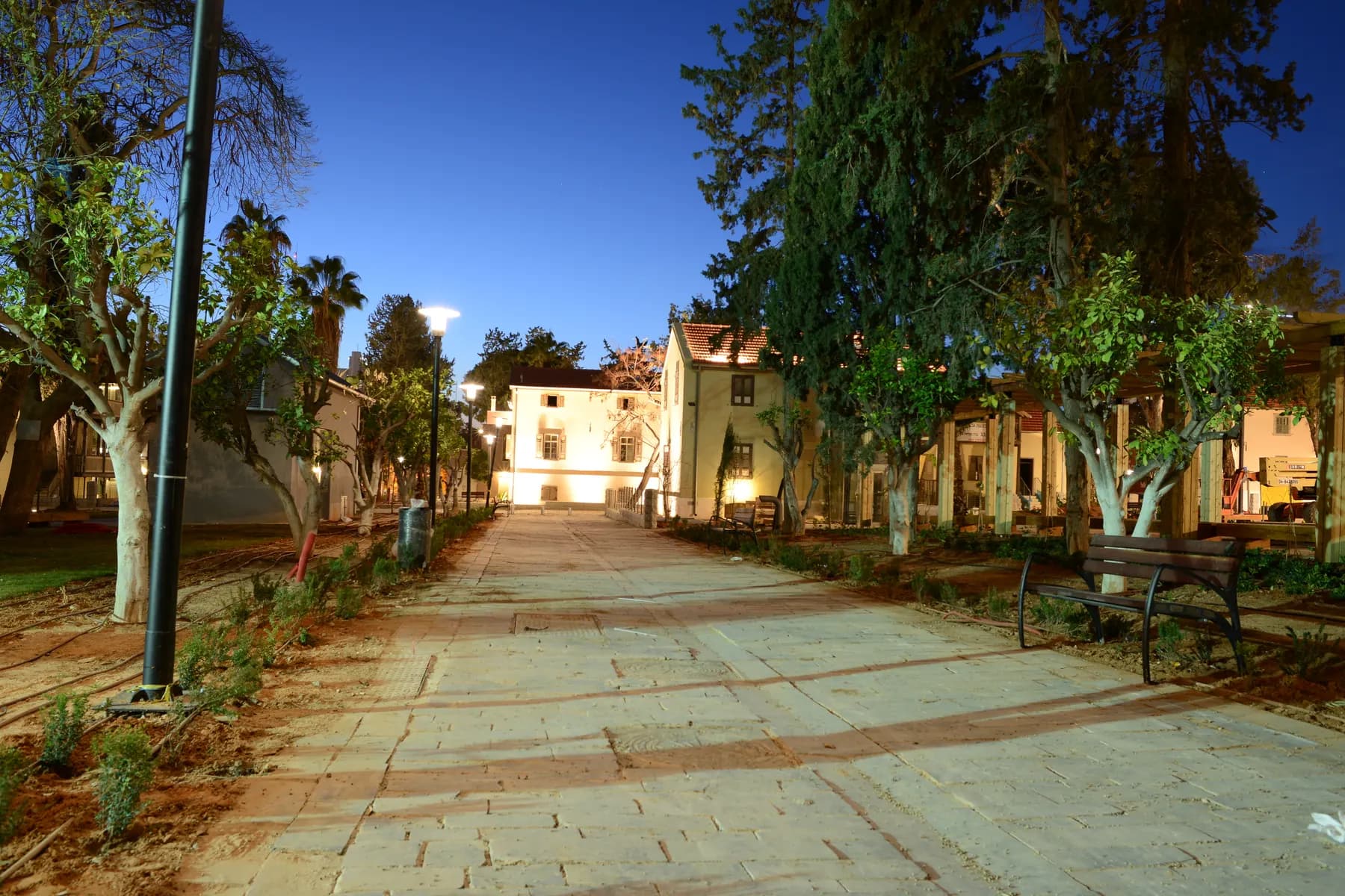 A paved avenue at dusk running between restored Templer houses and old trees, with a lit two-storey house at the far end