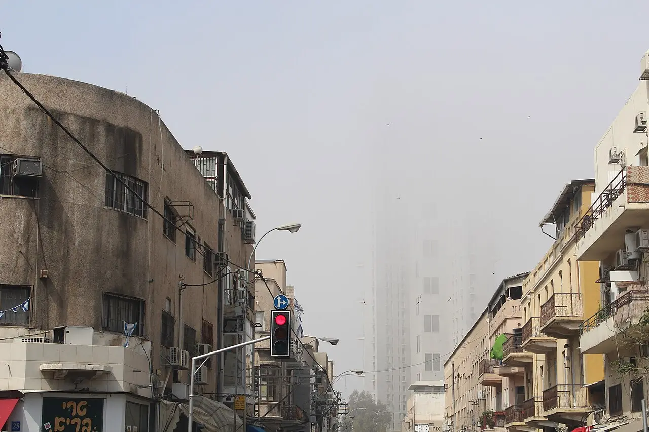 A street of low old buildings in Neve Tzedek, the Neve Tzedek Tower fading into mist behind them